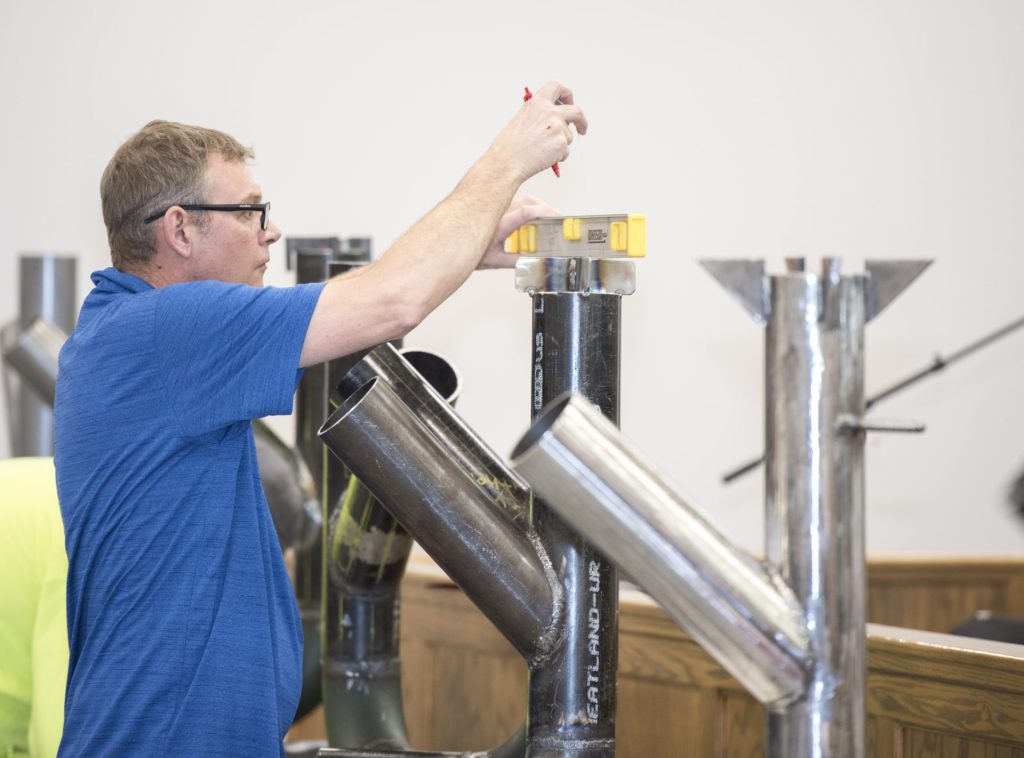 Image shows UA Local 400 member judging local students pipe stove in the Heat Up Your Future skills competition.